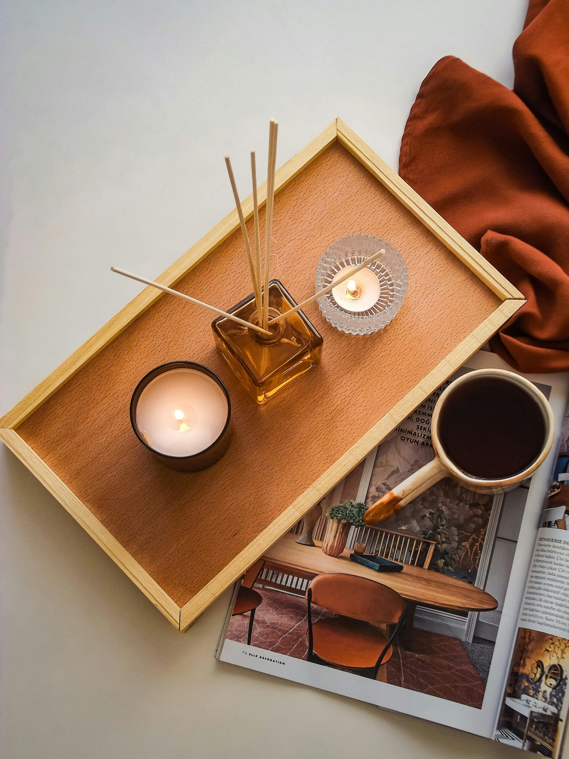 Top view of a relaxing tea setup with candles, incense, and magazine, creating a cozy ambiance.